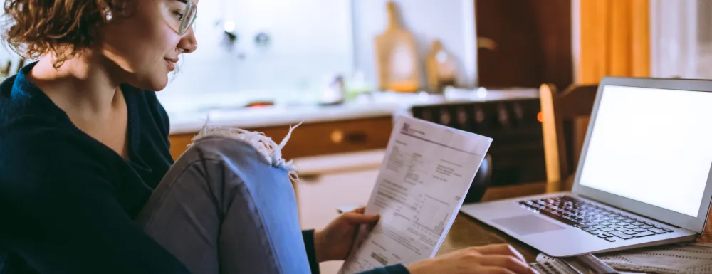 Stock image of a woman reading a bill and using laptop